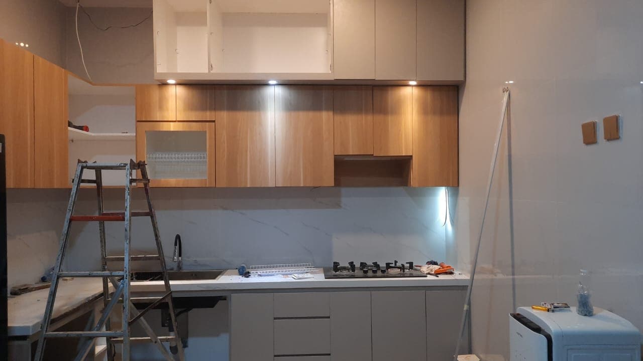 Proses renovasi dapur dengan kabinet kayu, meja putih, dan tangga lipat di depannya.