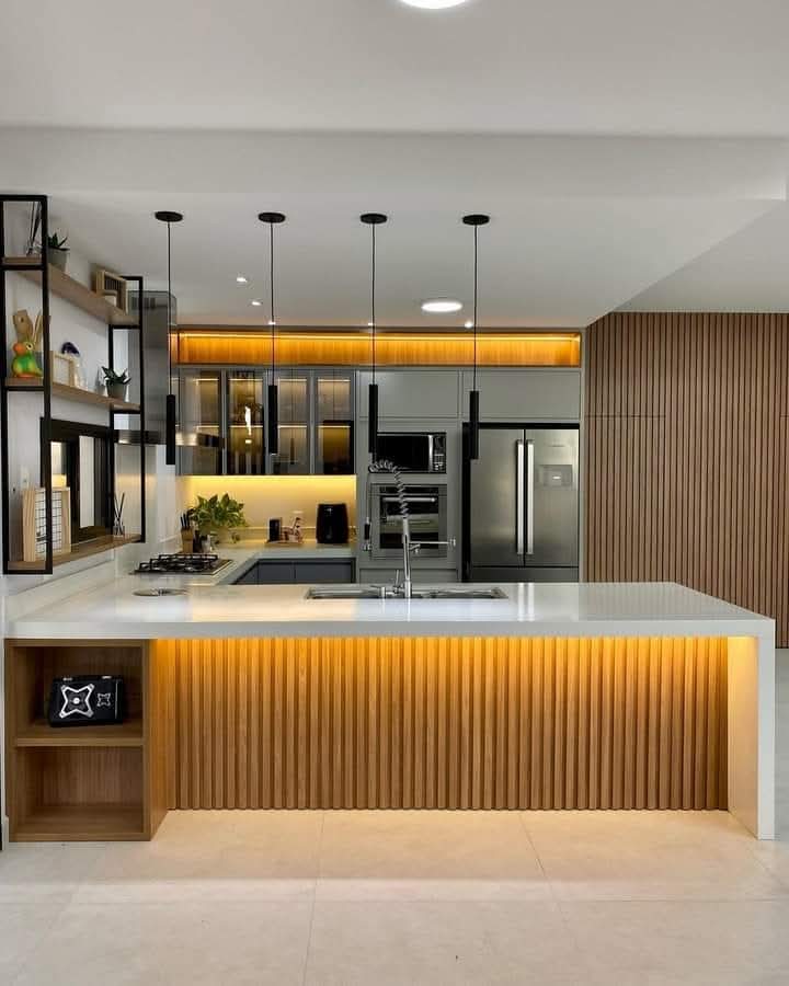Dapur modern dengan pulau berpanel kayu, pencahayaan LED hangat, meja putih, dan lampu gantung hitam.