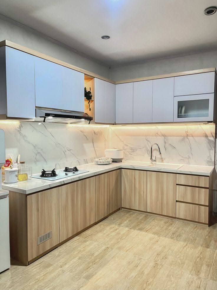 Dapur modern dengan kabinet biru muda, lemari kayu, backsplash marmer, dan pencahayaan bawah kabinet.