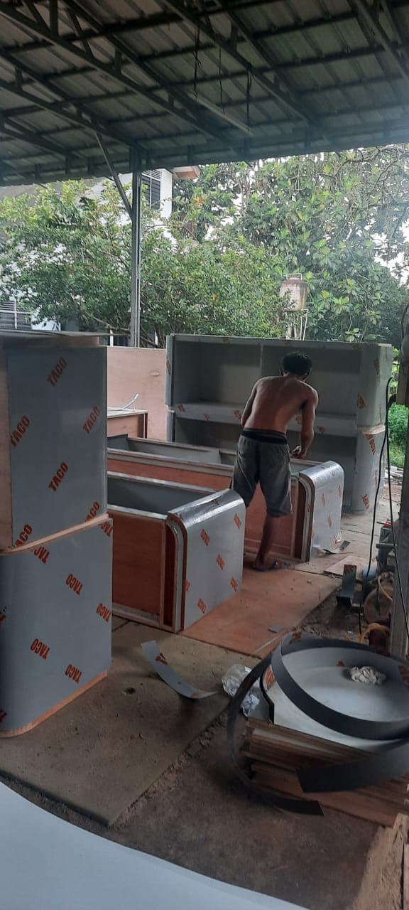 Seorang pria tanpa baju sedang merakit furnitur kayu berlapis pelindung abu-abu di bengkel terbuka.